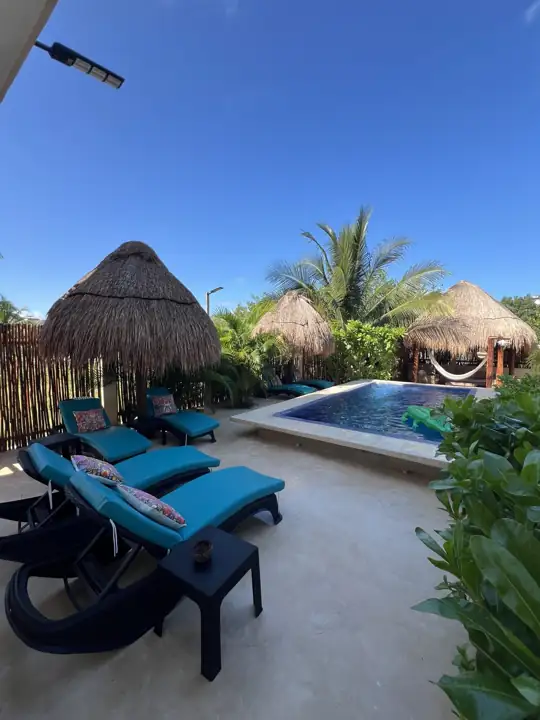 Turquoise pool loungers under a palapa with the swimming pool behind