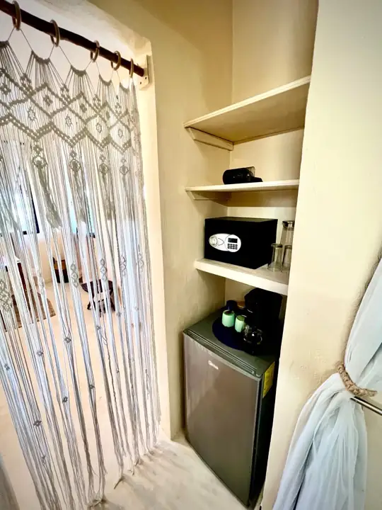 In-room mini refrigerator, safe and macramé curtain detail in a guest suite
